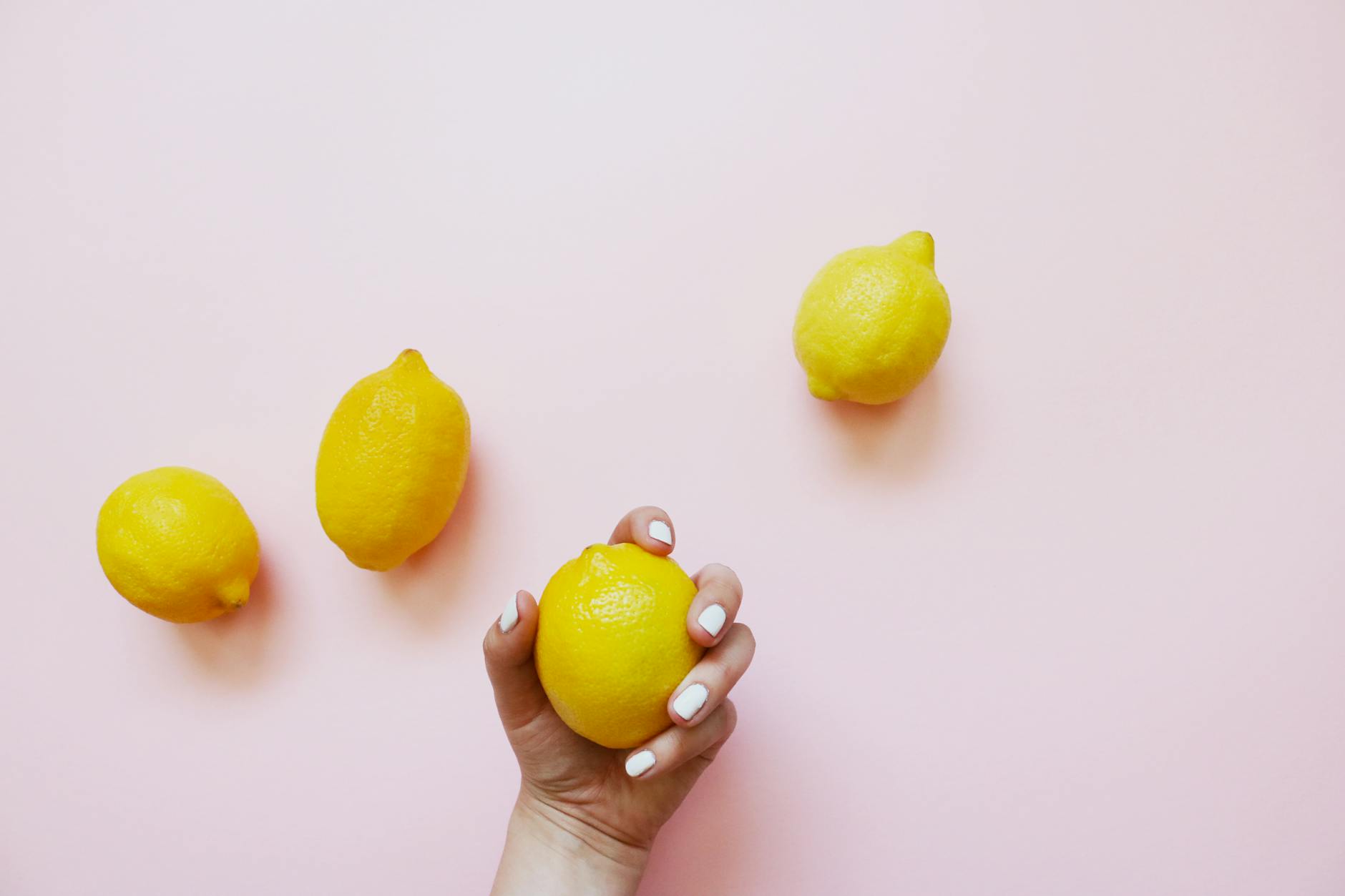 A hand holding a lemon against a soft pink background, symbolizing cyclical sensitivity shifts