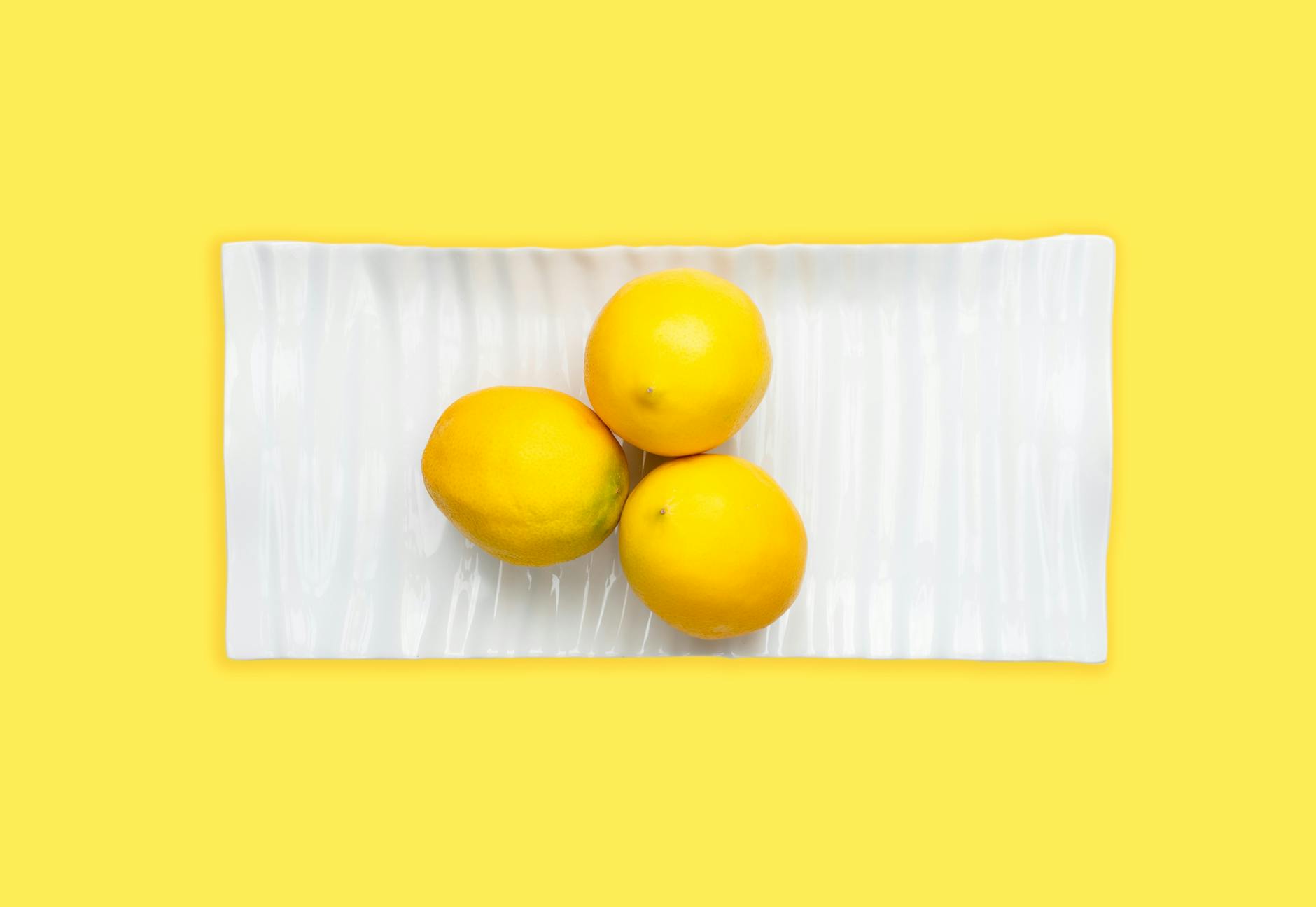 A hand holding a lemon against a soft pink background, symbolizing sensitive tissue and gentle care.