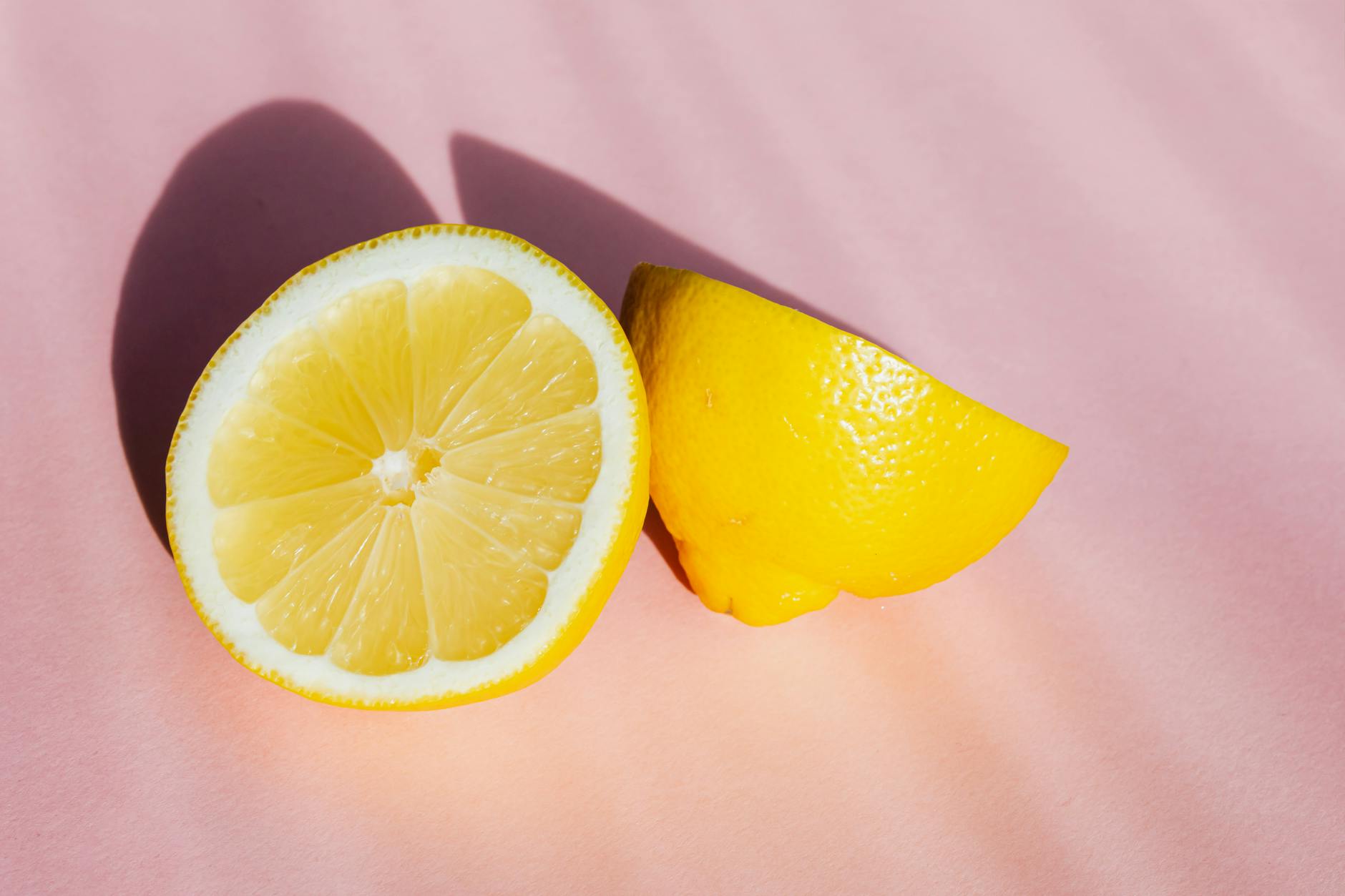 Fresh lemon halves arranged on a bright pink background, bathed in sunlight