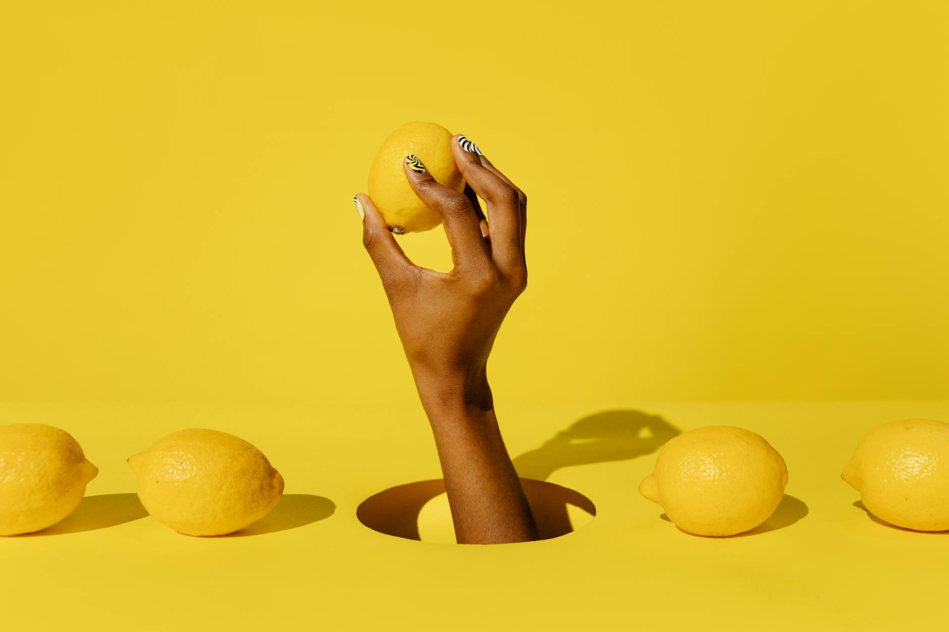 A hand holding a fresh lemon against a vivid yellow background, symbolizing renewed vitality and pleasure