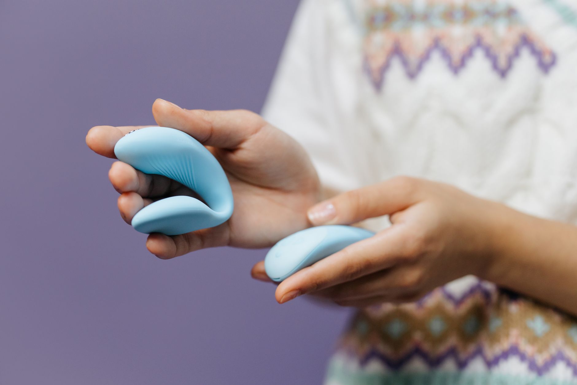 Eine Frau hält einen blauen Vibrator in der Hand vor lila Hintergrund, was Selbstvergnügen und Selbstliebe symbolisiert