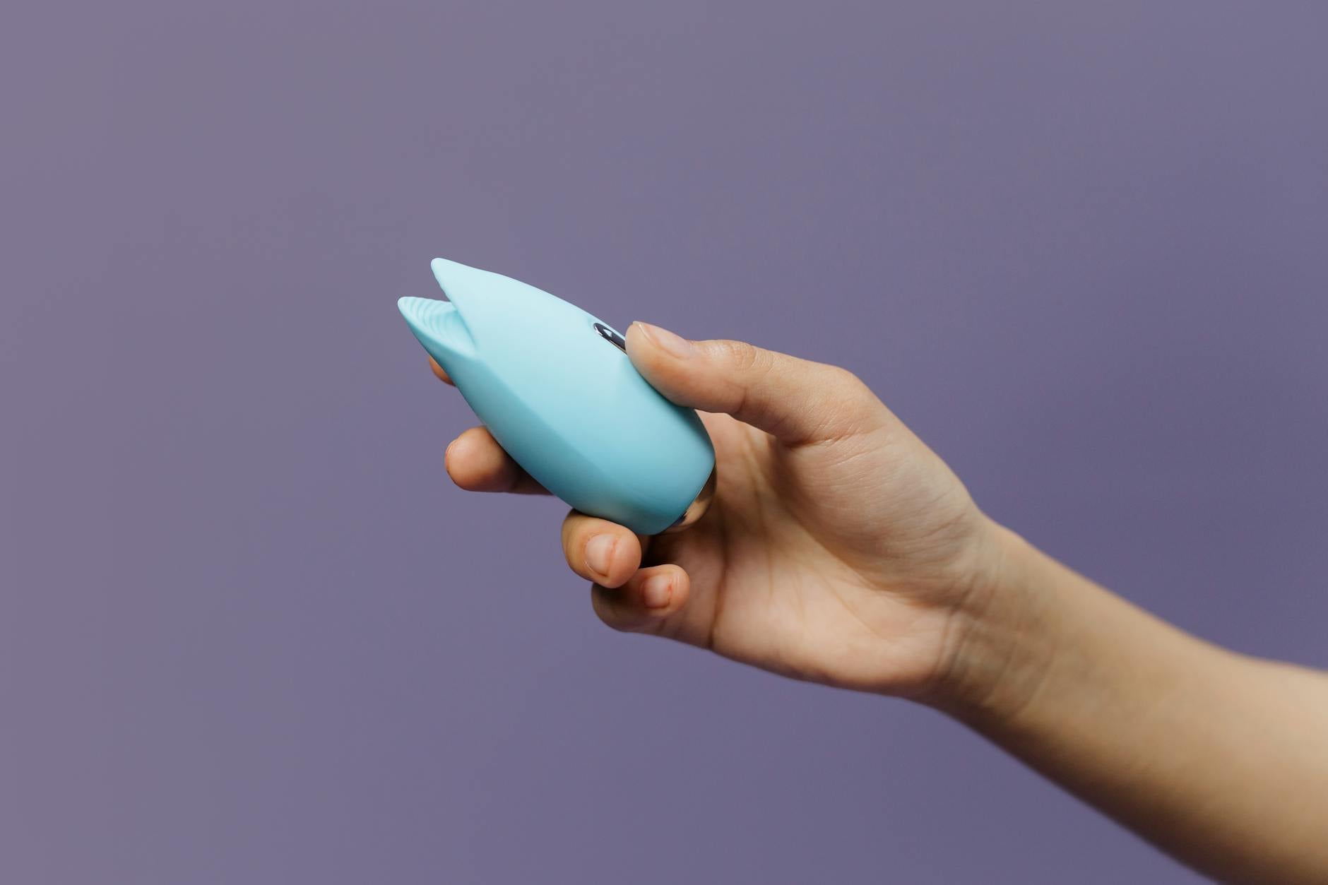 A blue silicone sex toy held in hand against a purple background, promoting self-love and sexuality.