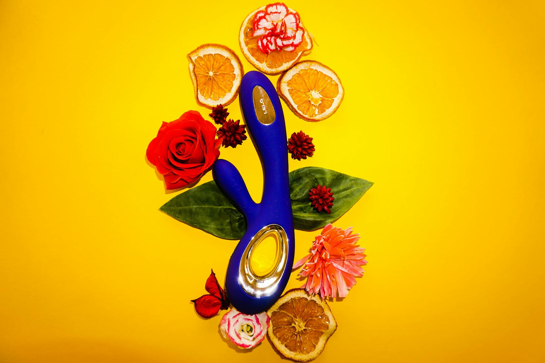 A hand reaching over a variety of colorful sex toys arranged on a table.