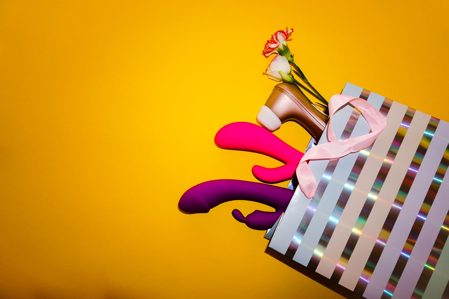 Colorful vibrators with flowers in a holistic gift arrangement against a bright yellow background