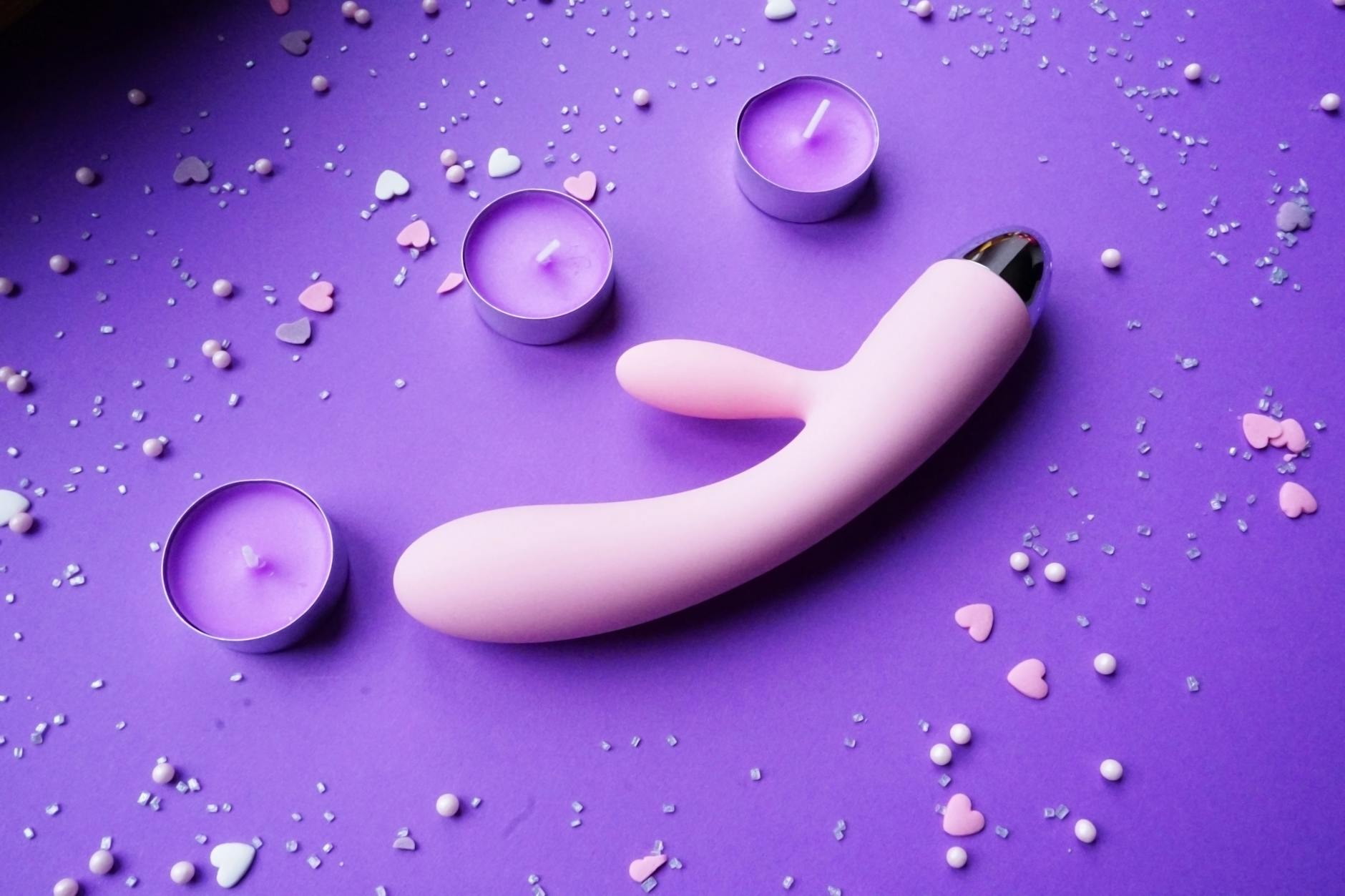 Pink lemon vibrator on purple background with heart confetti and candles for a romantic vibe